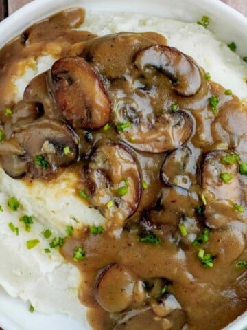 Homemade mushroom gravy with browned baby bella mushrooms spooned over creamy mashed potatoes and garnished with fresh chives.