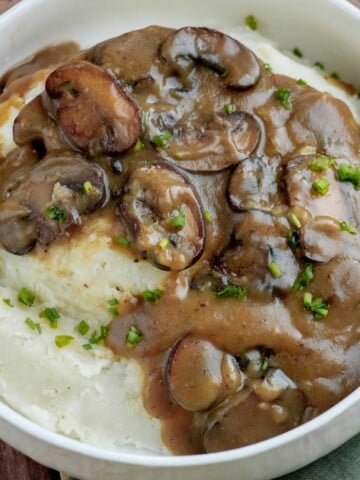 Homemade mushroom gravy with browned baby bella mushrooms spooned over creamy mashed potatoes and garnished with fresh chives.