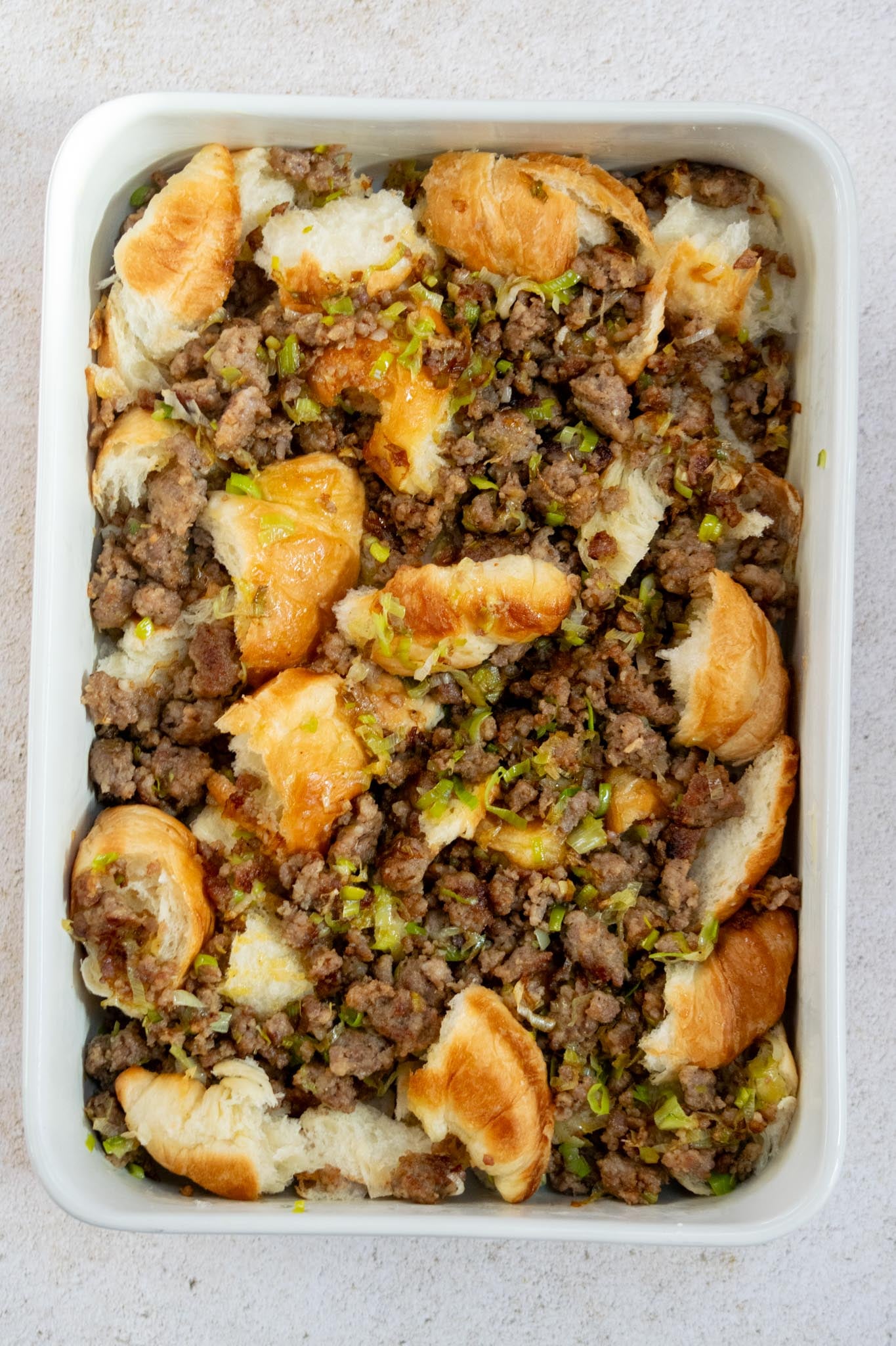 Layer the casserole. Tear the croissants into bite-size pieces and spread them in a greased 9x13-inch baking dish. Spoon the sausage and leek mixture evenly over the top.