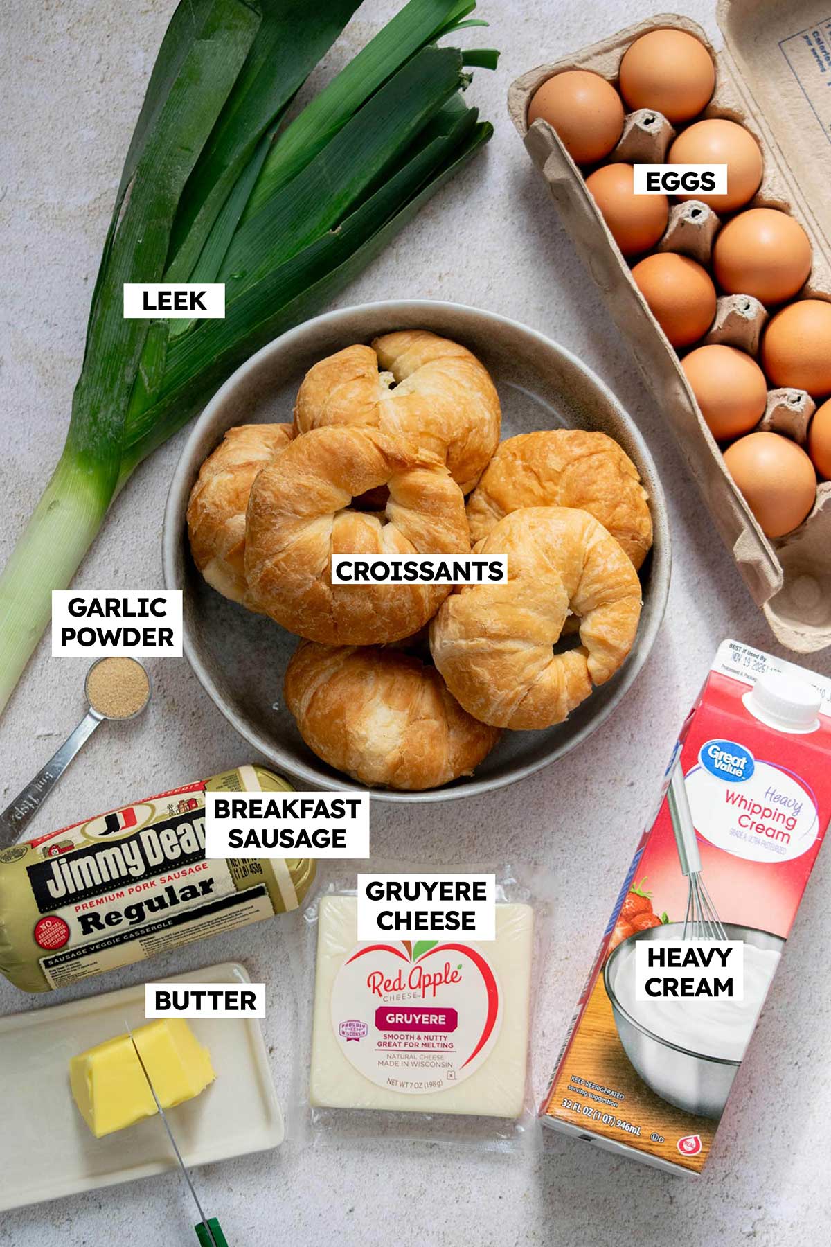 Ingredients for croissant breakfast casserole including croissants, breakfast sausage, eggs, leeks, heavy cream and Gruyère cheese.