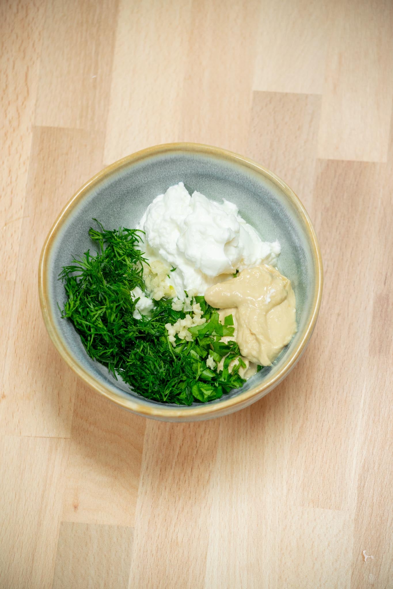 Chop the dill and parsley, and mince the garlic. Add to a bowl with the lemon juice, Greek yogurt and hummus.
