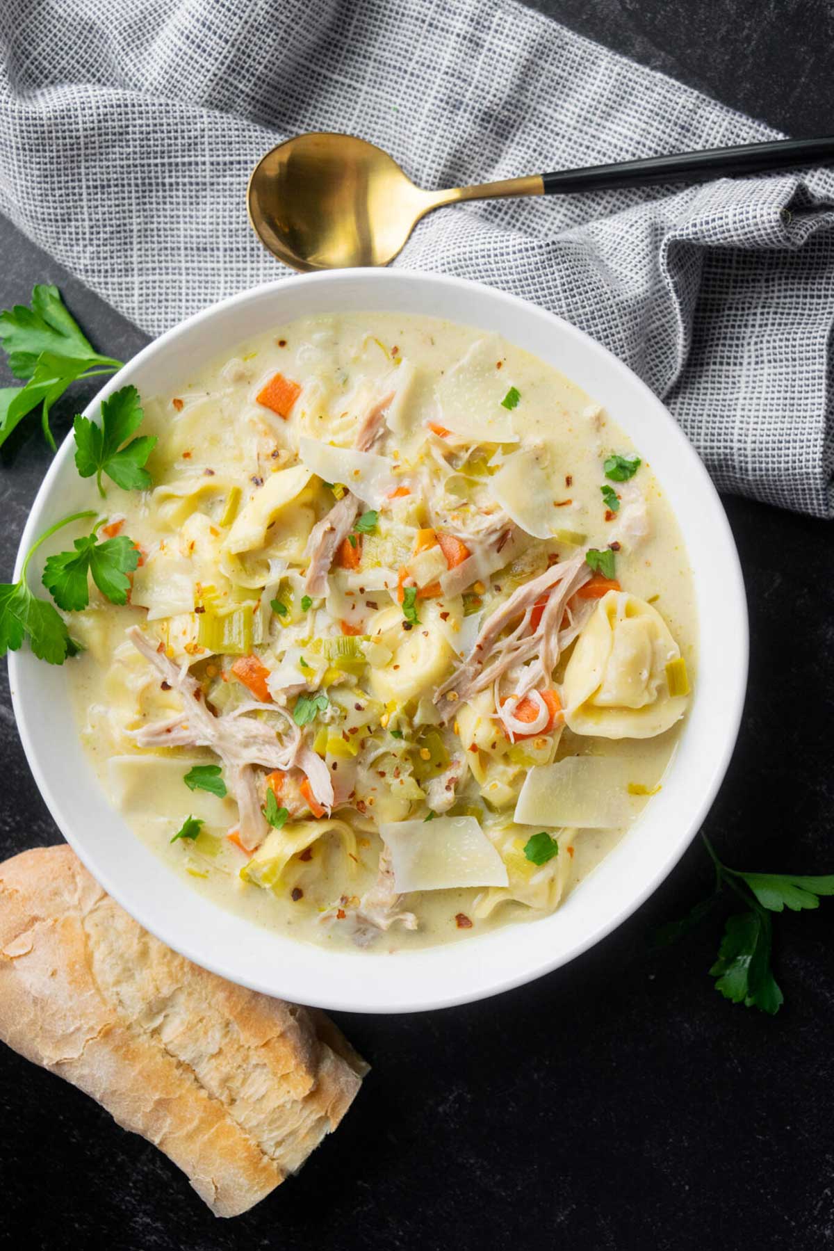 Creamy chicken tortellini soup with leeks, shredded chicken, carrots, Parmesan, parsley, and crusty bread.