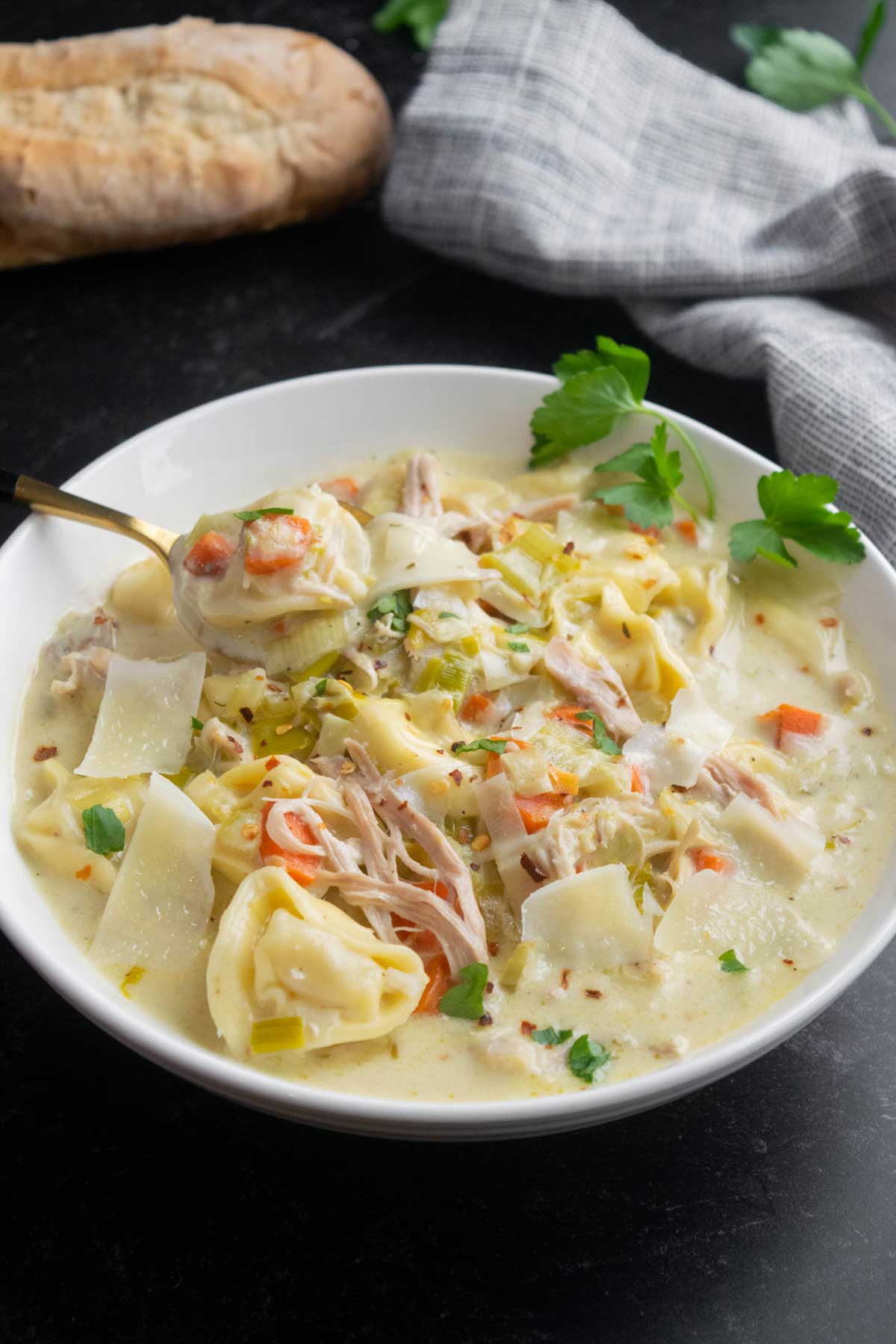Creamy chicken tortellini soup with leeks and shredded chicken, with a spoonful of tortellini and vegetables lifted from the bowl.
