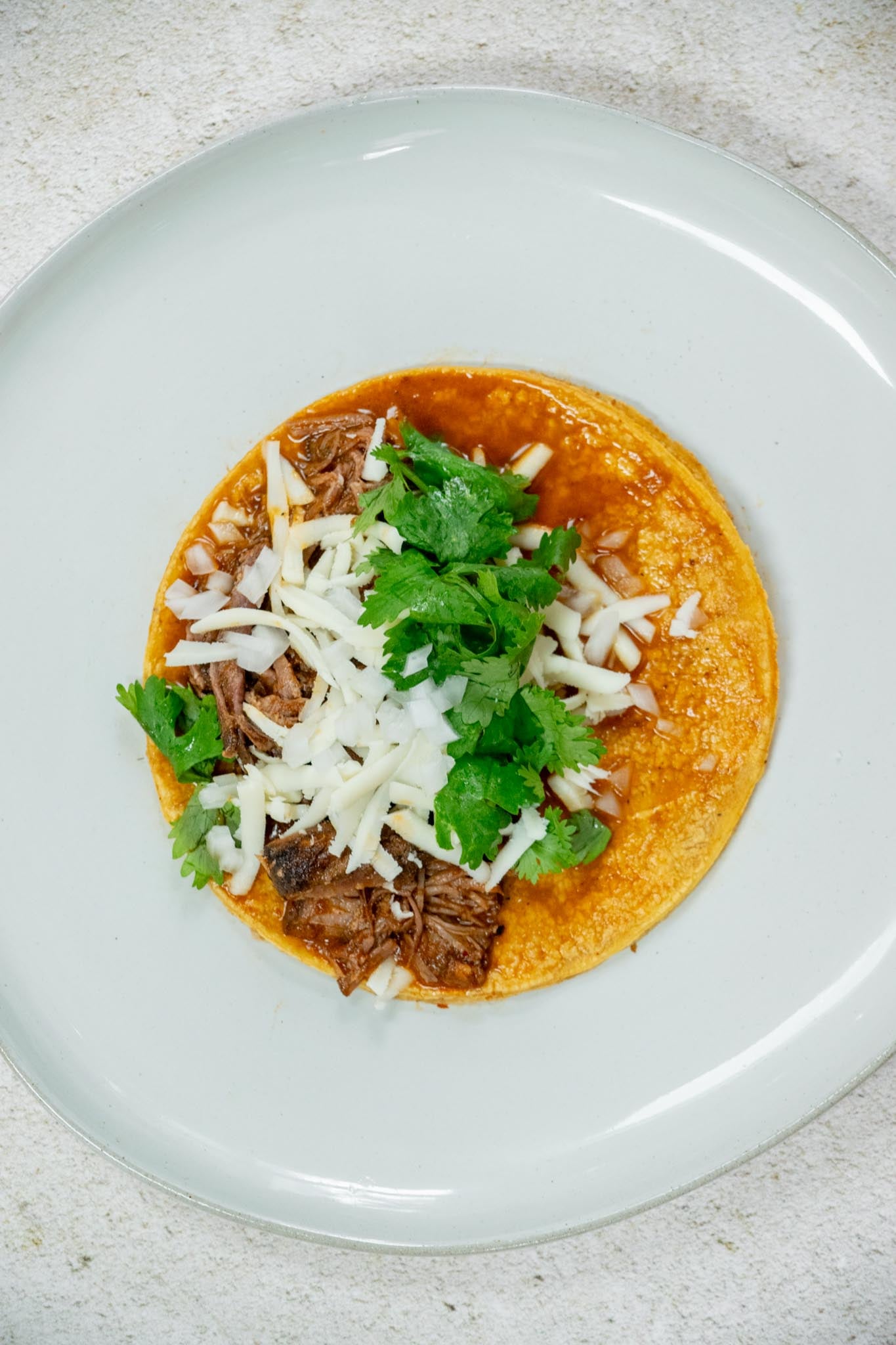 Build your tacos. Layer on oaxaca cheese, sauced beef, finely diced onion, and cilantro leaves.