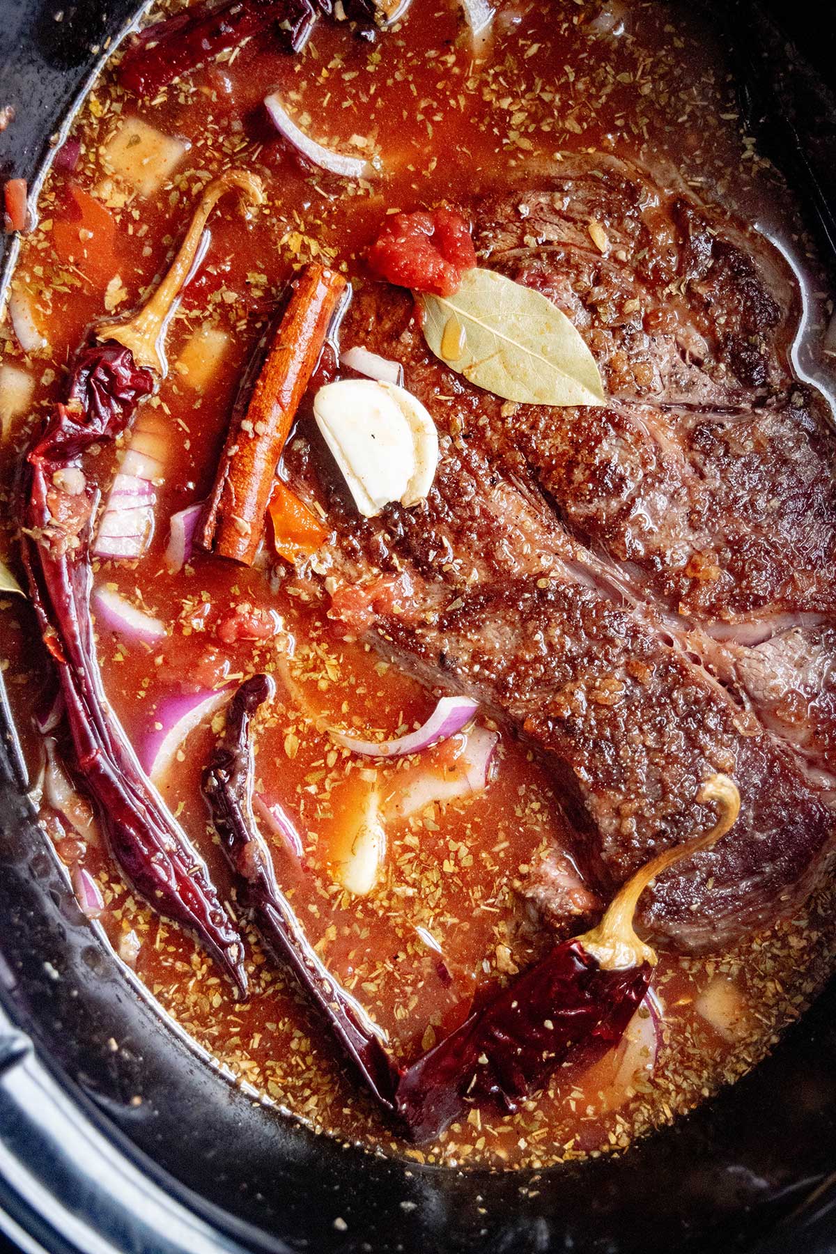 Add everything to the slow cooker. Place the seared beef in the Crock Pot with the dried chiles, onion, garlic, chipotle peppers, broth, vinegar, and spices.