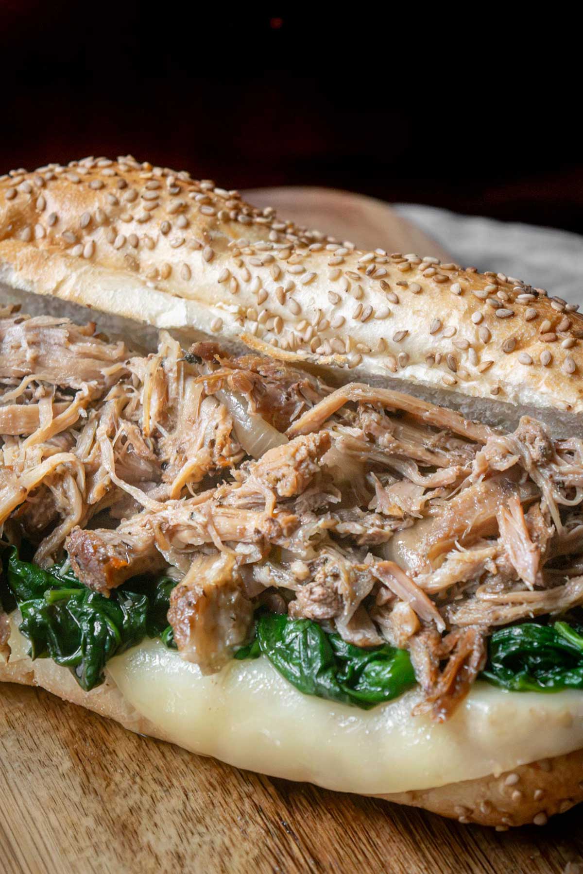 Close-up of a South Philly Italian roast pork sandwich loaded with tender shredded pork, garlicky spinach, and melted provolone on a sesame-seeded Italian roll.