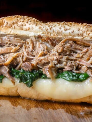 Close-up of a South Philly Italian roast pork sandwich stuffed with tender shredded pork, garlicky spinach, and melted provolone cheese on a seeded hoagie roll.