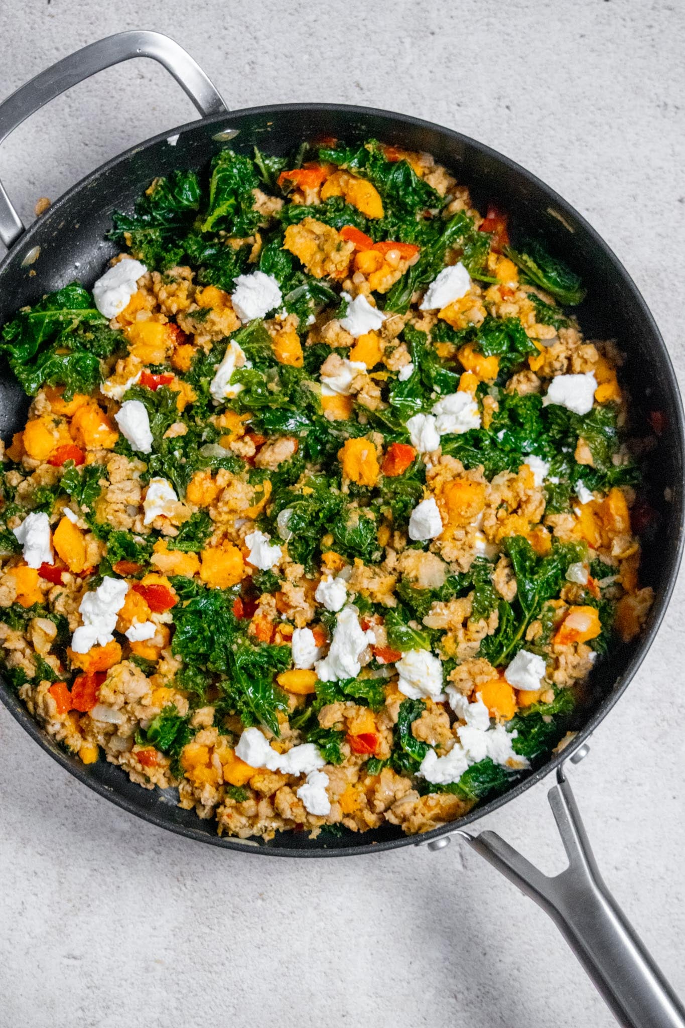 Finish and serve. Increase the heat to medium and stir in the fresh garlic. Cook for about 1 minute, just until fragrant. Remove the skillet from the heat, top with crumbled goat cheese, and serve warm.