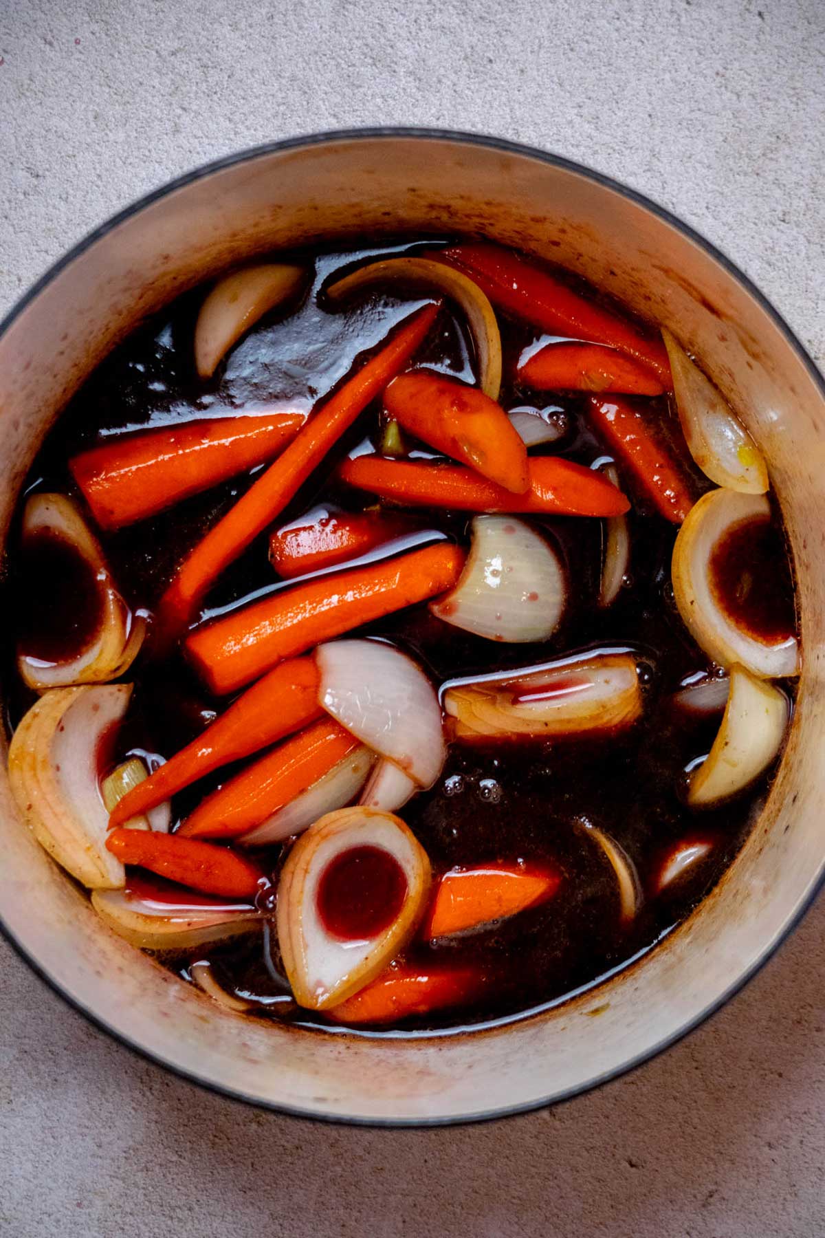 Once the vegetables are lightly browned, pour in the red wine and use a wooden spoon or spatula to scrape up any browned bits from the bottom of the pot.