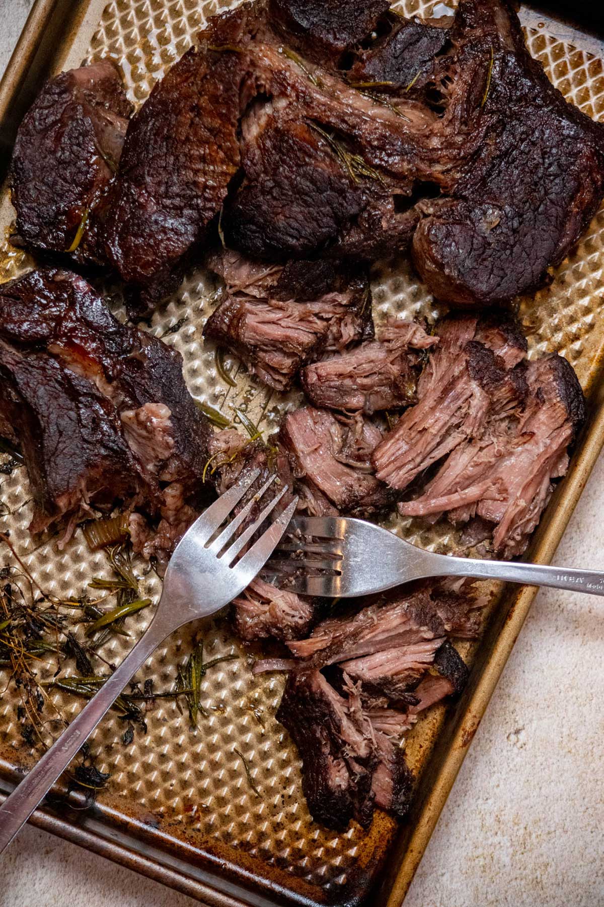 Remove the beef from the Dutch oven with tongs and transfer it to a plate or sheet pan. Discard the rosemary and thyme, then shred the beef with two forks, removing any large pieces of fat or connective tissue.