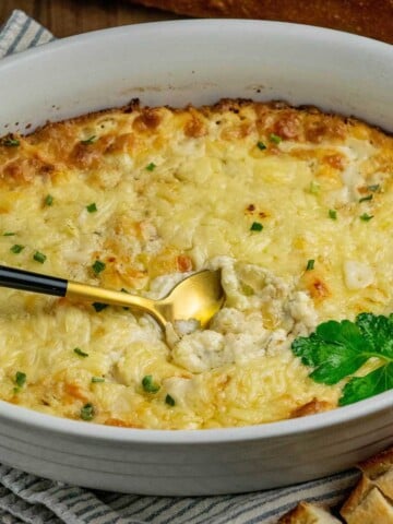 Hot and cheesy French onion soup dip with caramelized onions, golden melted cheese, and fresh herbs in a white baking dish with a spoon and crusty baguette slices.