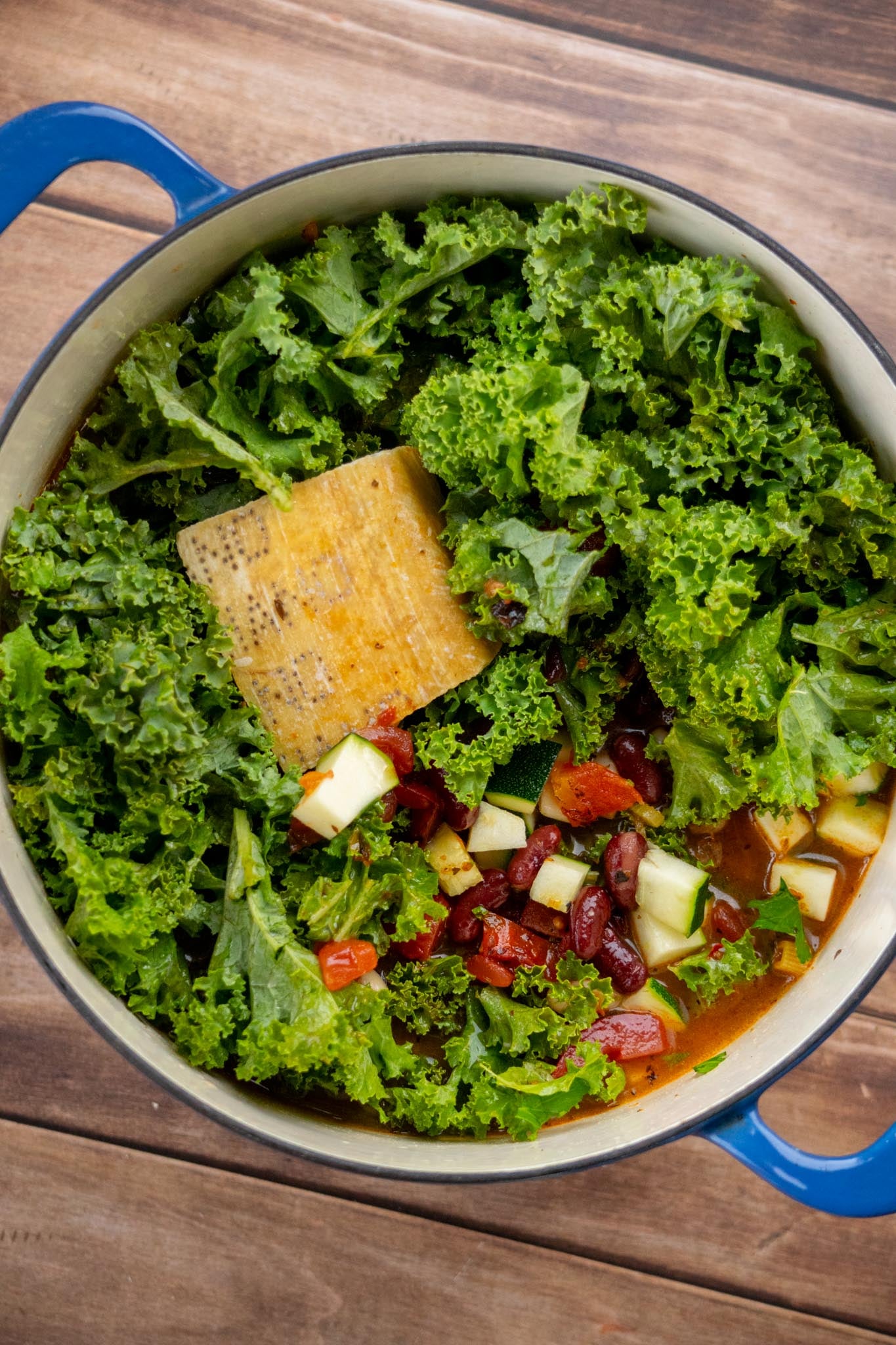 Add the remaining ingredients. Stir in the zucchini, diced tomatoes, vegetable broth, bay leaves, parsley, water, kale, pasta, and beans. Add a vegetarian-friendly hard cheese rind, if using.