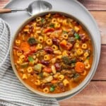 Overhead view of a bowl of vegetarian minestrone soup with cubetti pasta, zucchini, carrots, kidney beans, and cannellini beans in a rich tomato broth, garnished with fresh parsley.