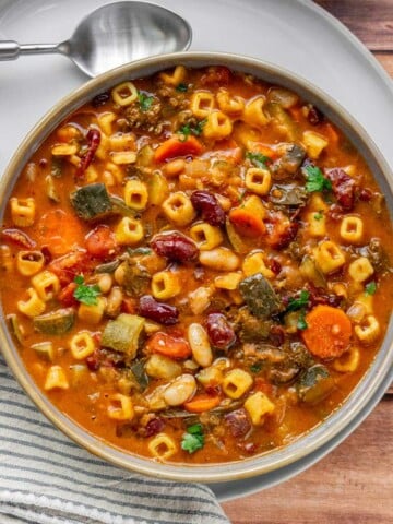 Overhead view of a bowl of vegetarian minestrone soup with cubetti pasta, zucchini, carrots, kidney beans, and cannellini beans in a rich tomato broth, garnished with fresh parsley.