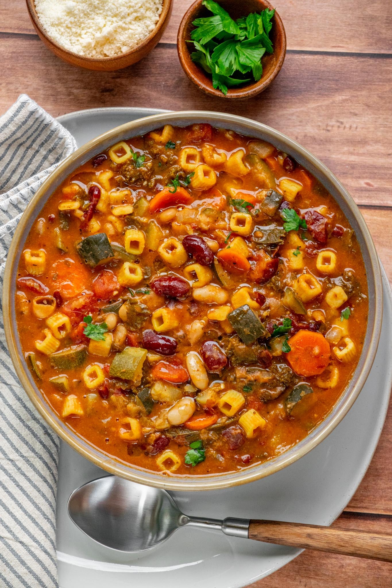Overhead view of vegetarian minestrone soup with cubetti pasta, zucchini, carrots, kidney beans, and cannellini beans in a rich tomato broth, garnished with fresh parsley.