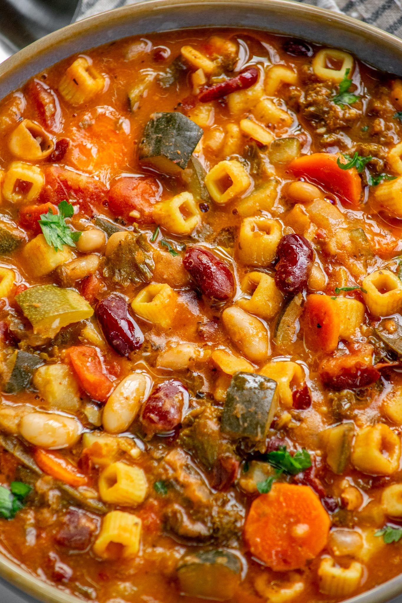 Close-up of vegetarian minestrone soup with cubetti pasta, zucchini, carrots, kidney beans, and cannellini beans in a rich tomato broth.
