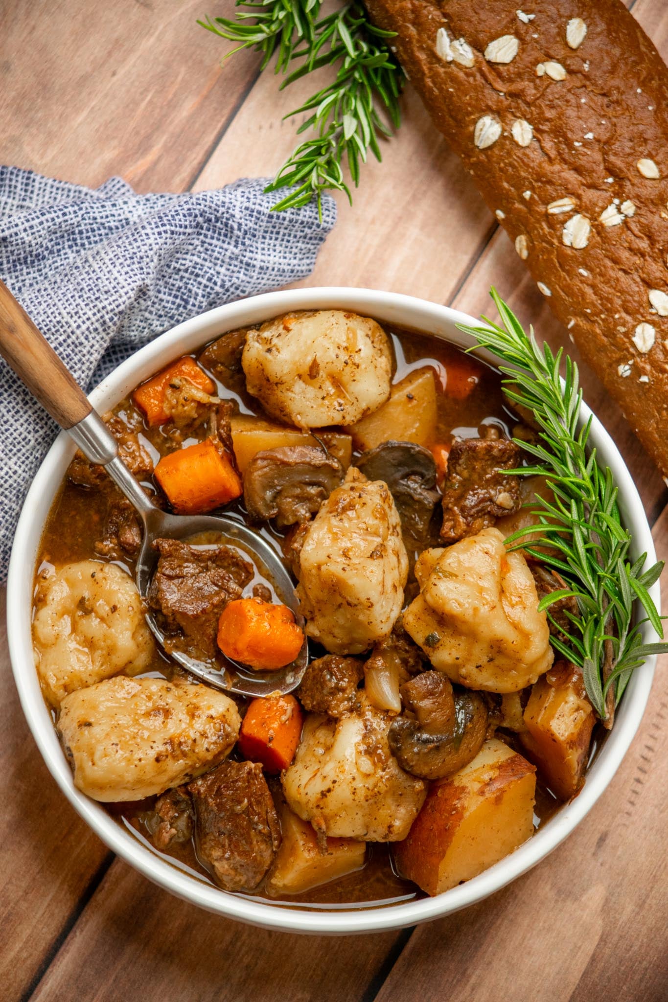 Overhead view of slow cooker beef stew with dumplings, tender chuck roast, vegetables, and biscuit dumplings in savory gravy, garnished with fresh rosemary.