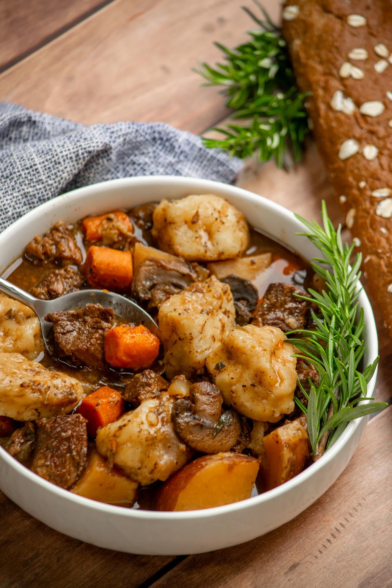 Slow cooker beef stew and dumplings with tender beef, carrots, red potatoes, mushrooms, and fluffy biscuit dumplings in a rich gravy, served with a spoon.