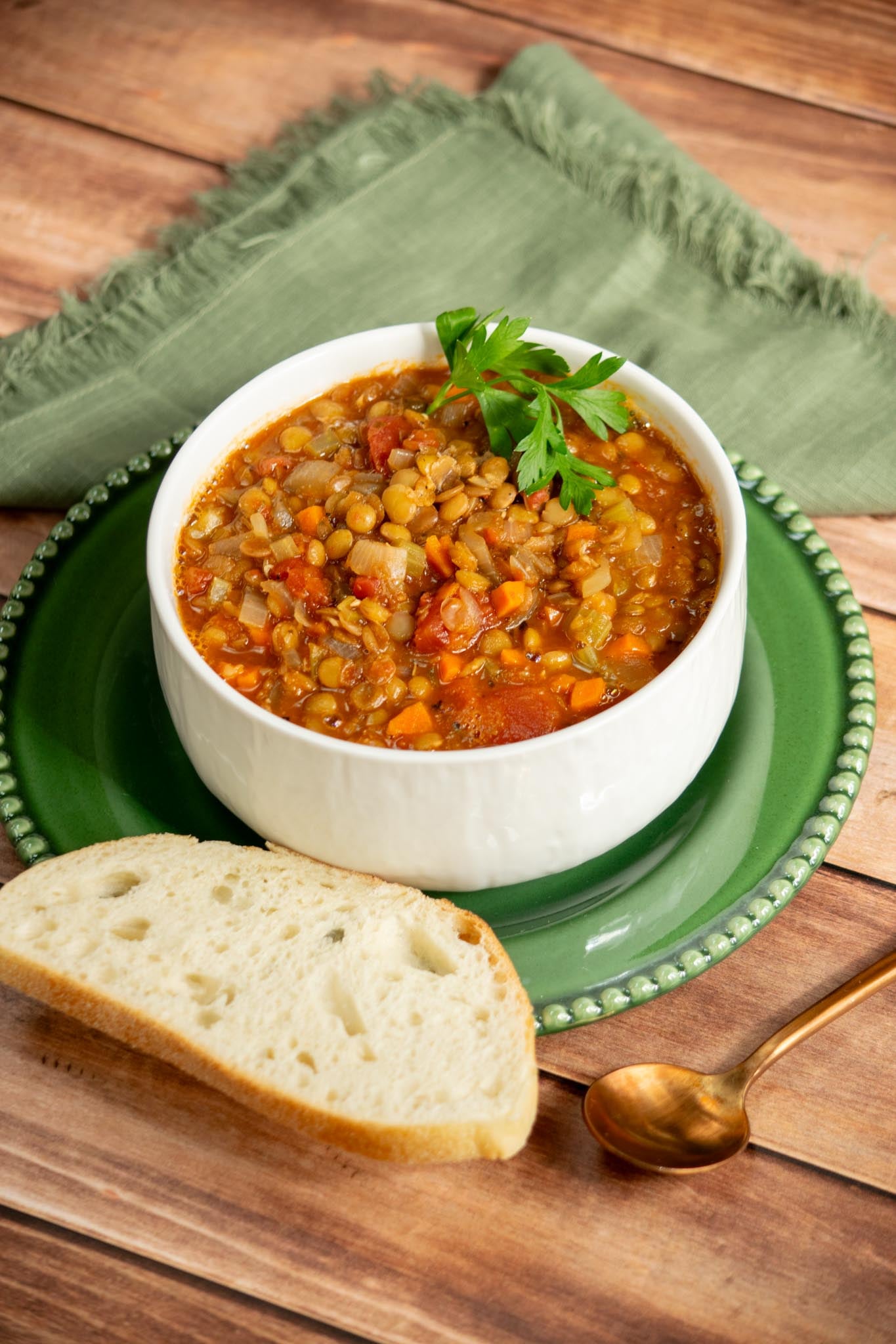 Easy green lentil soup with carrots, celery, fire-roasted tomatoes, and parsley served with crusty bread on a green plate.