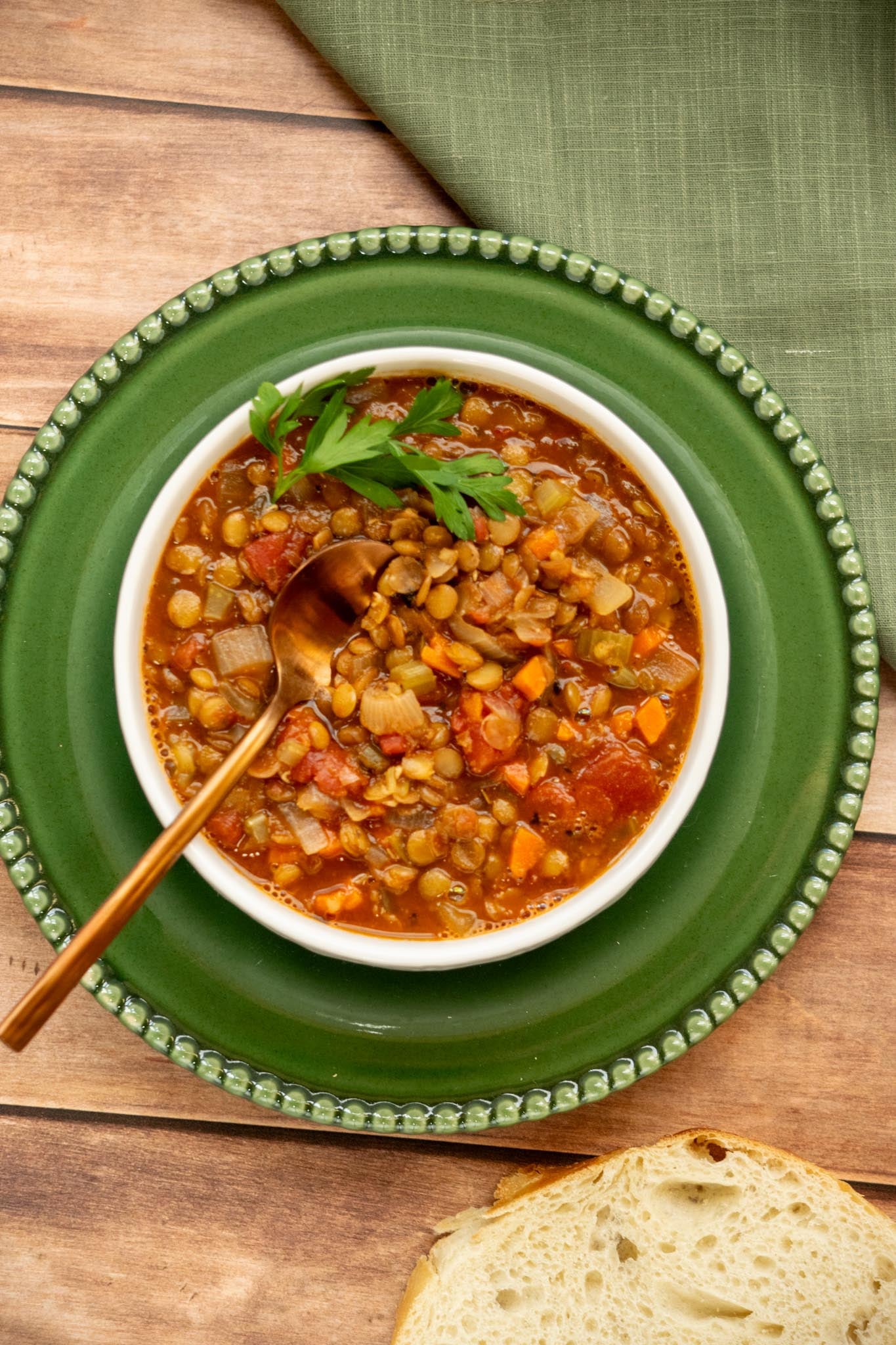 Overhead view of easy green lentil soup with carrots, celery, fire-roasted tomatoes, parsley, and a spoon in the bowl.