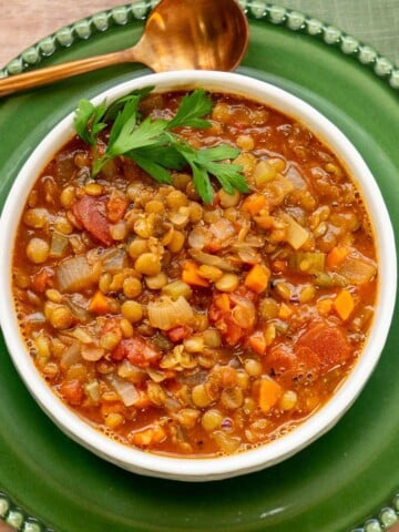 Easy green lentil soup with carrots, celery, fire-roasted tomatoes, and parsley in a white bowl.