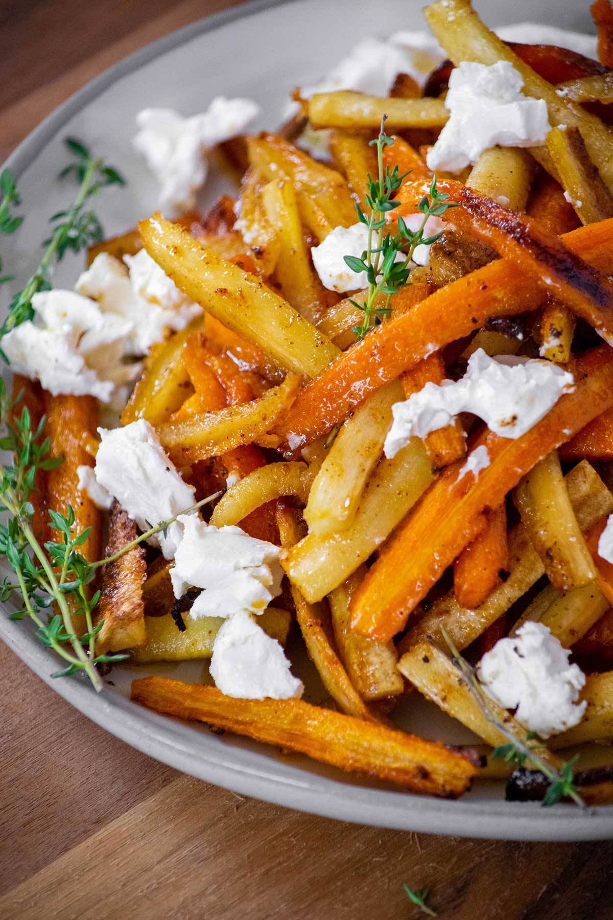 Honey roasted parsnips and carrots with caramelized edges, crumbled goat cheese, and fresh thyme on a serving plate.
