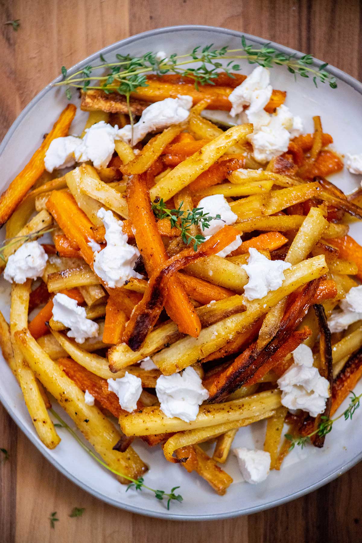 Overhead view of honey roasted parsnips and carrots topped with creamy goat cheese and fresh thyme.