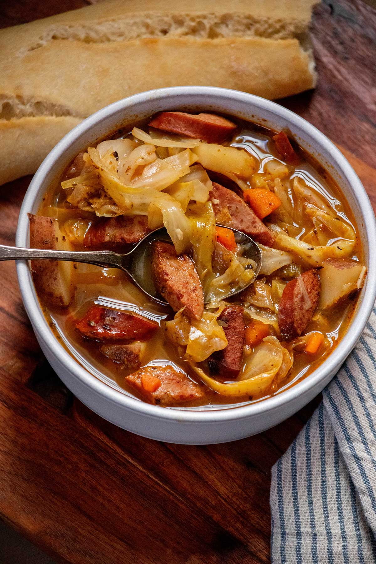 Cabbage soup with sausage, potatoes, carrots and green cabbage served in a bowl with a spoonful of kielbasa and cabbage.