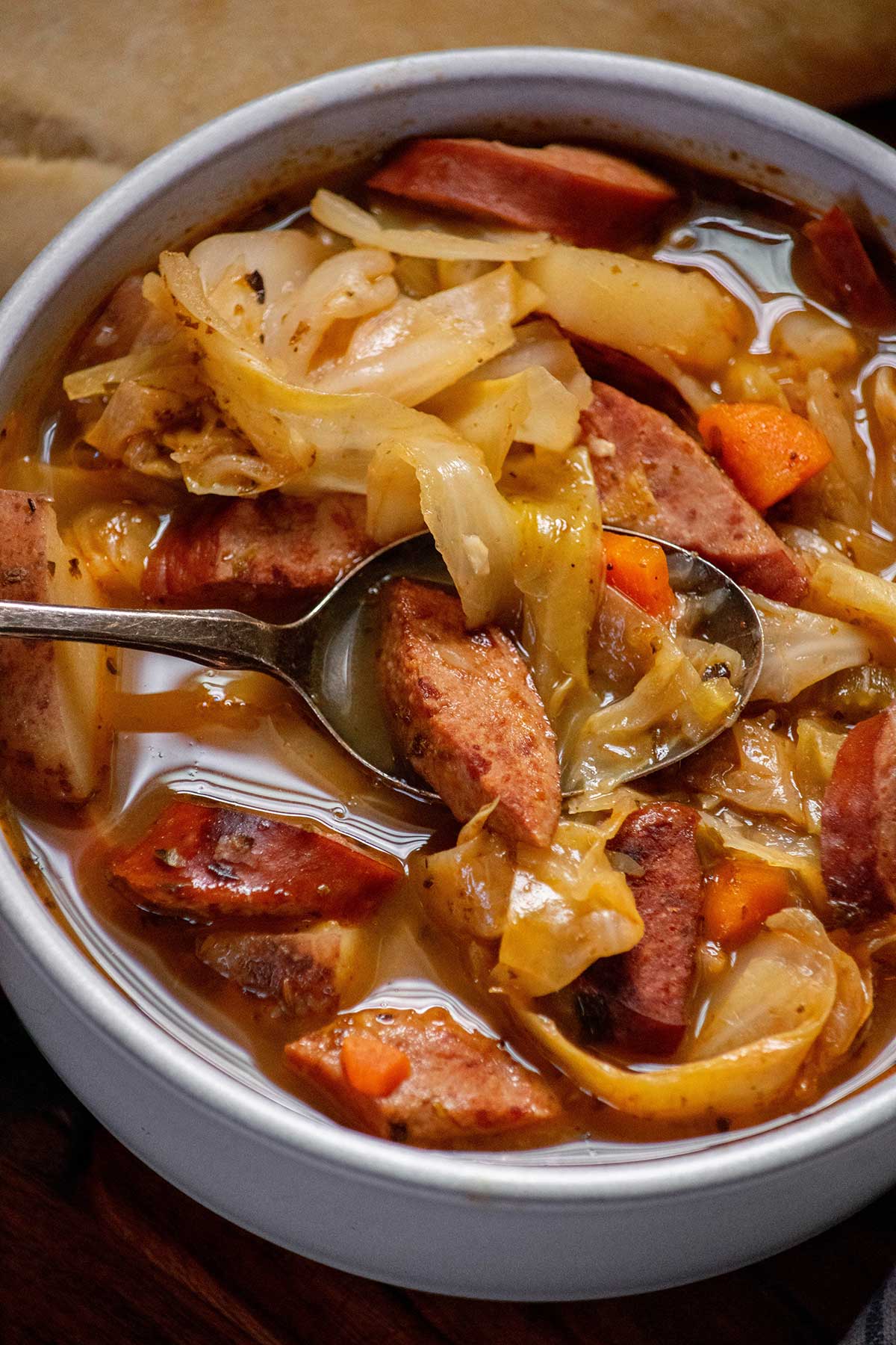 Close-up of cabbage soup with sausage, showing browned kielbasa, tender cabbage, red potatoes and carrots in broth.