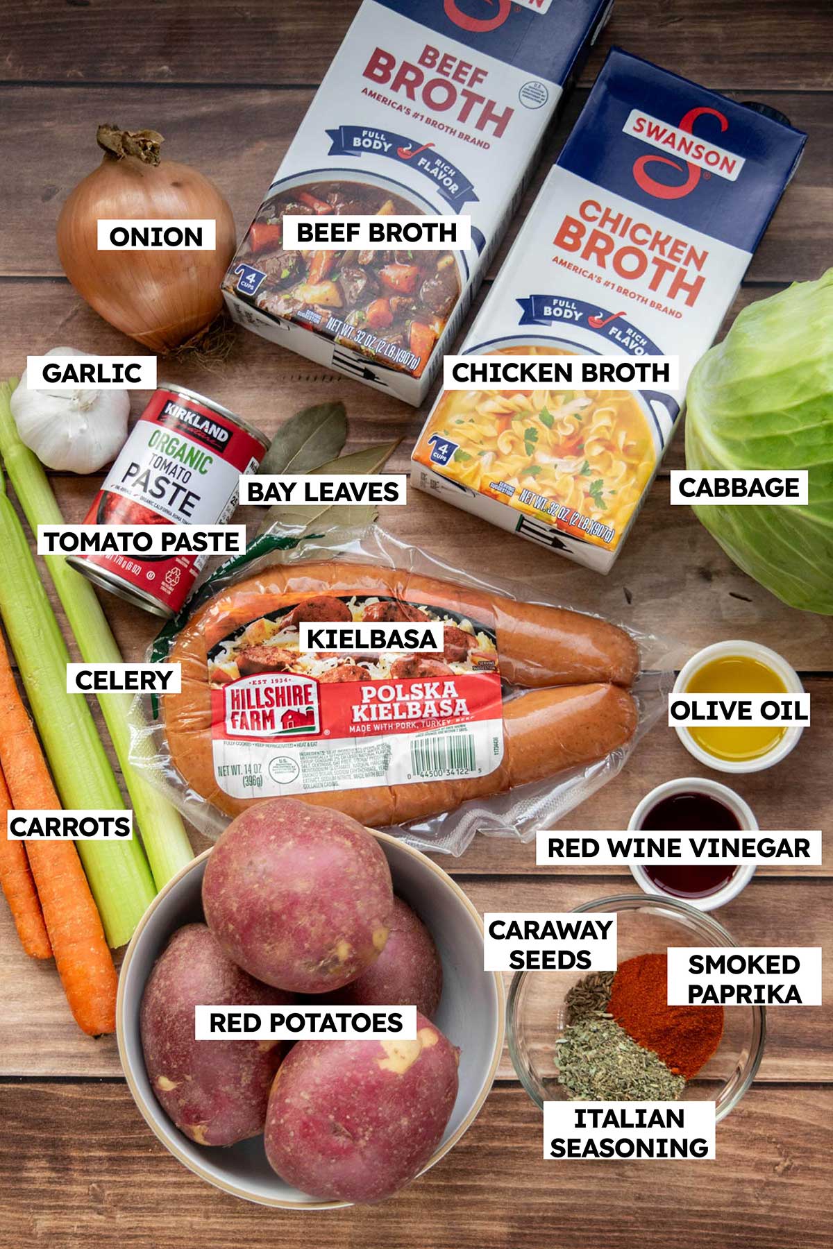 Ingredients for cabbage soup with sausage including kielbasa, cabbage, red potatoes, carrots, celery, onion, garlic, tomato paste, beef broth and chicken broth.