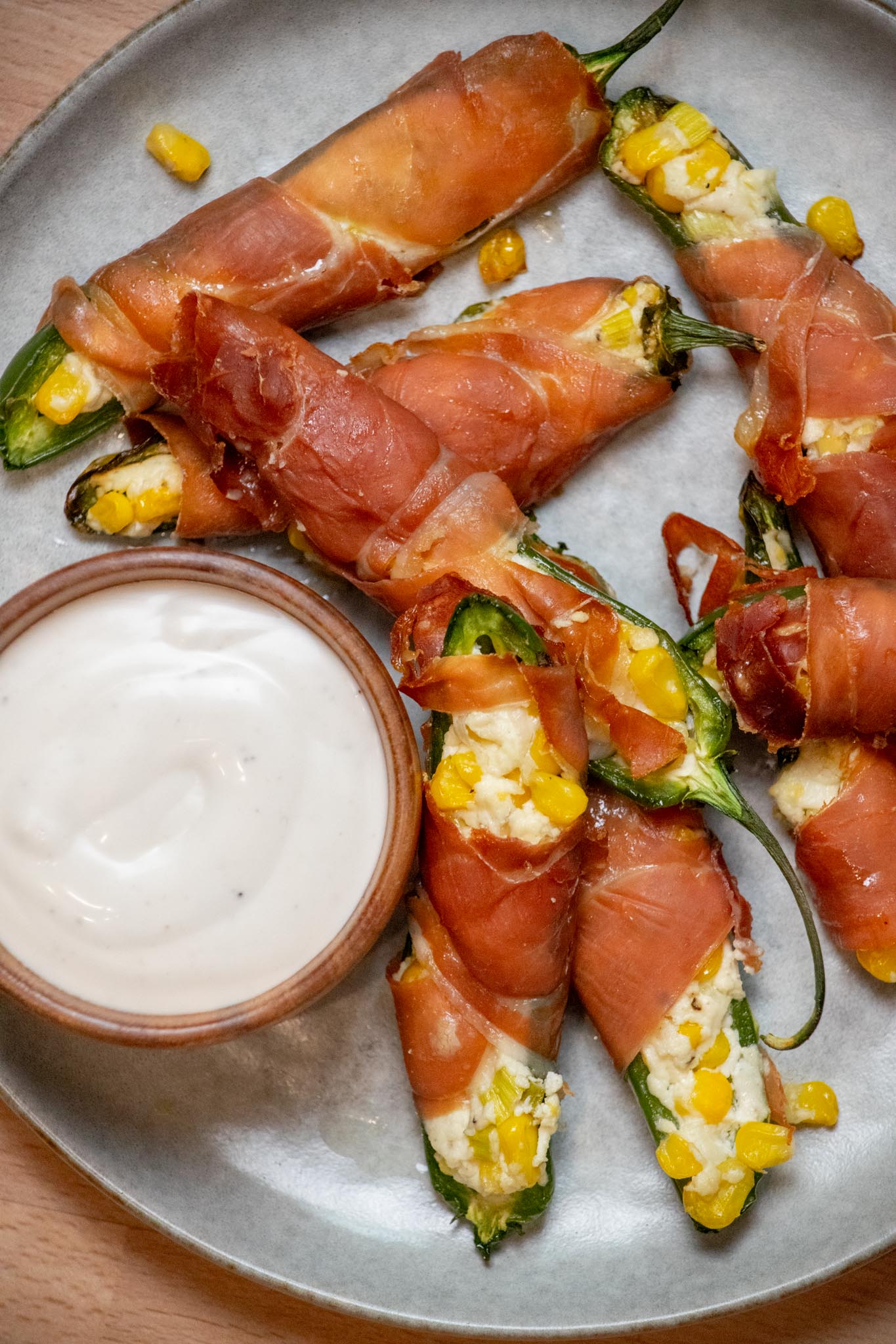 Closeup view of Goat Cheese Jalapeño Poppers with Prosciutto and Sweet Corn on a pate with a bowl of ranch..