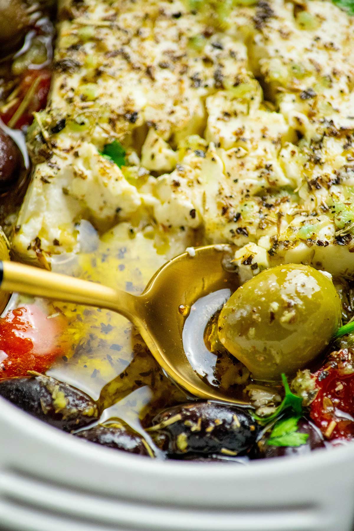 Close-up view on baked feta with olive, spooning out of dish.