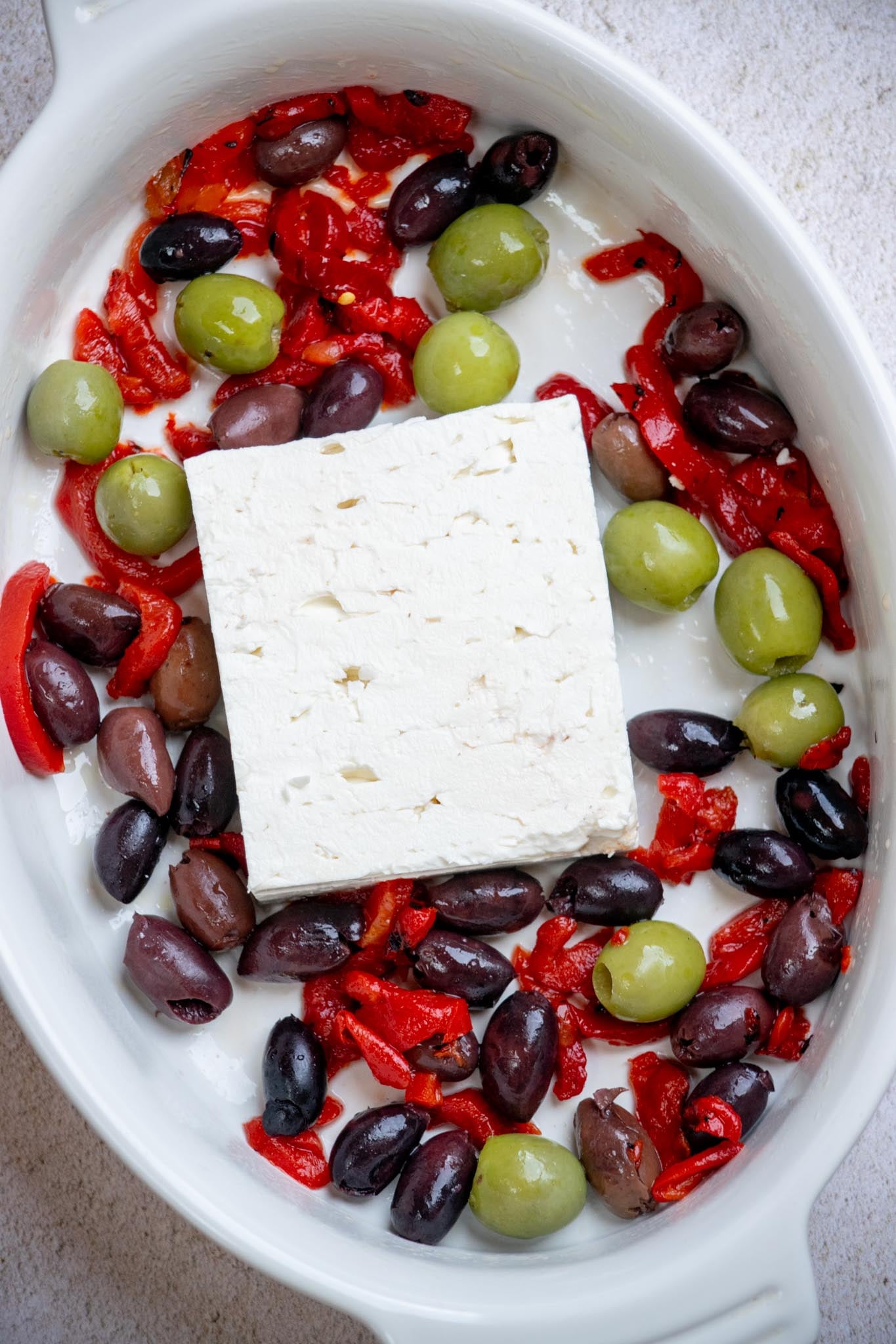 Preheat the oven to 350°. Grease a baking dish with olive oil, then add feta to the center, and arrange olives and red peppers around the outside.