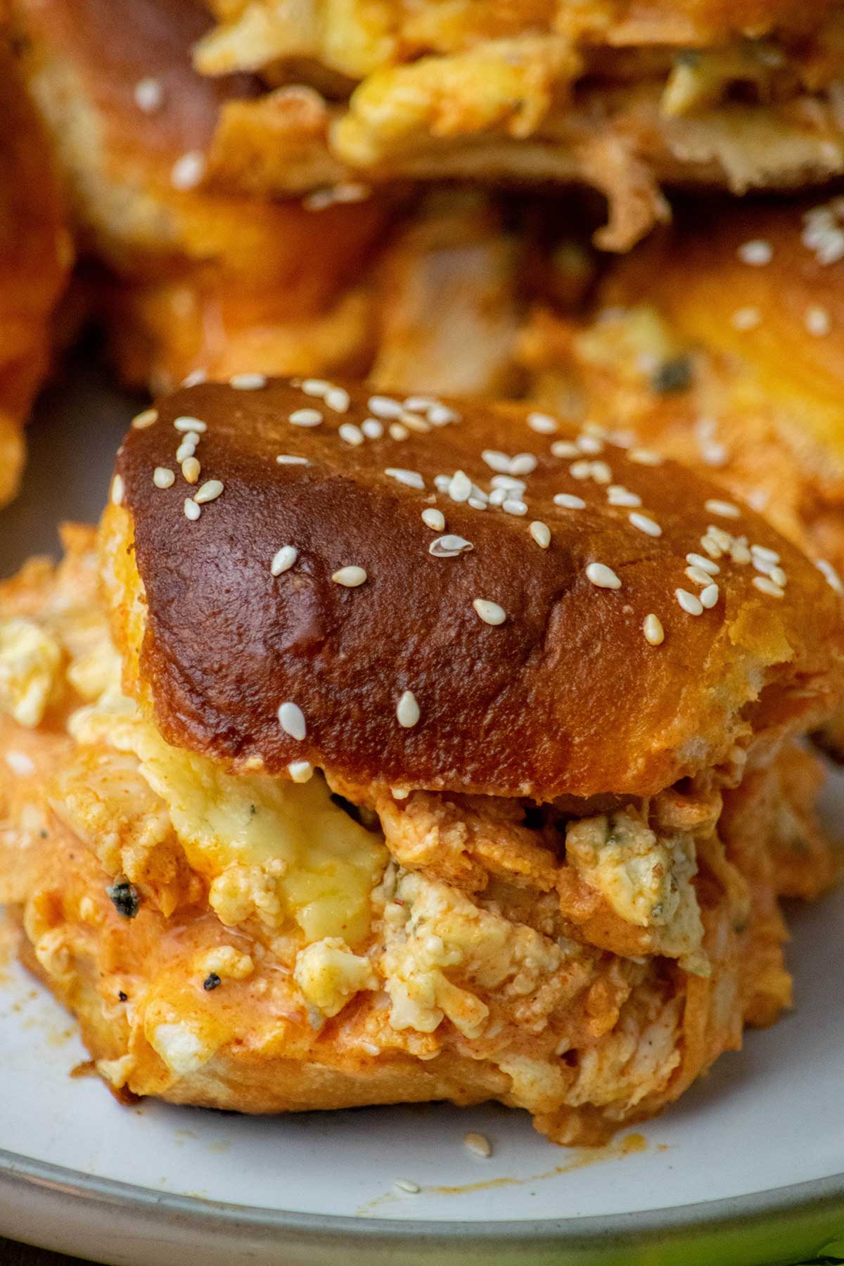 Close-up of a Buffalo chicken slider filled with spicy shredded chicken, melted cheese, and blue cheese on a toasted sesame roll.