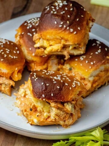 Buffalo Chicken Sliders with shredded buffalo chicken, melted cheese, blue cheese crumbles, and sesame-topped Hawaiian rolls on a serving plate.