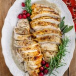 Sliced Crockpot turkey breast with golden herb-seasoned skin and homemade onion gravy, garnished with fresh rosemary, sage, and cranberries.