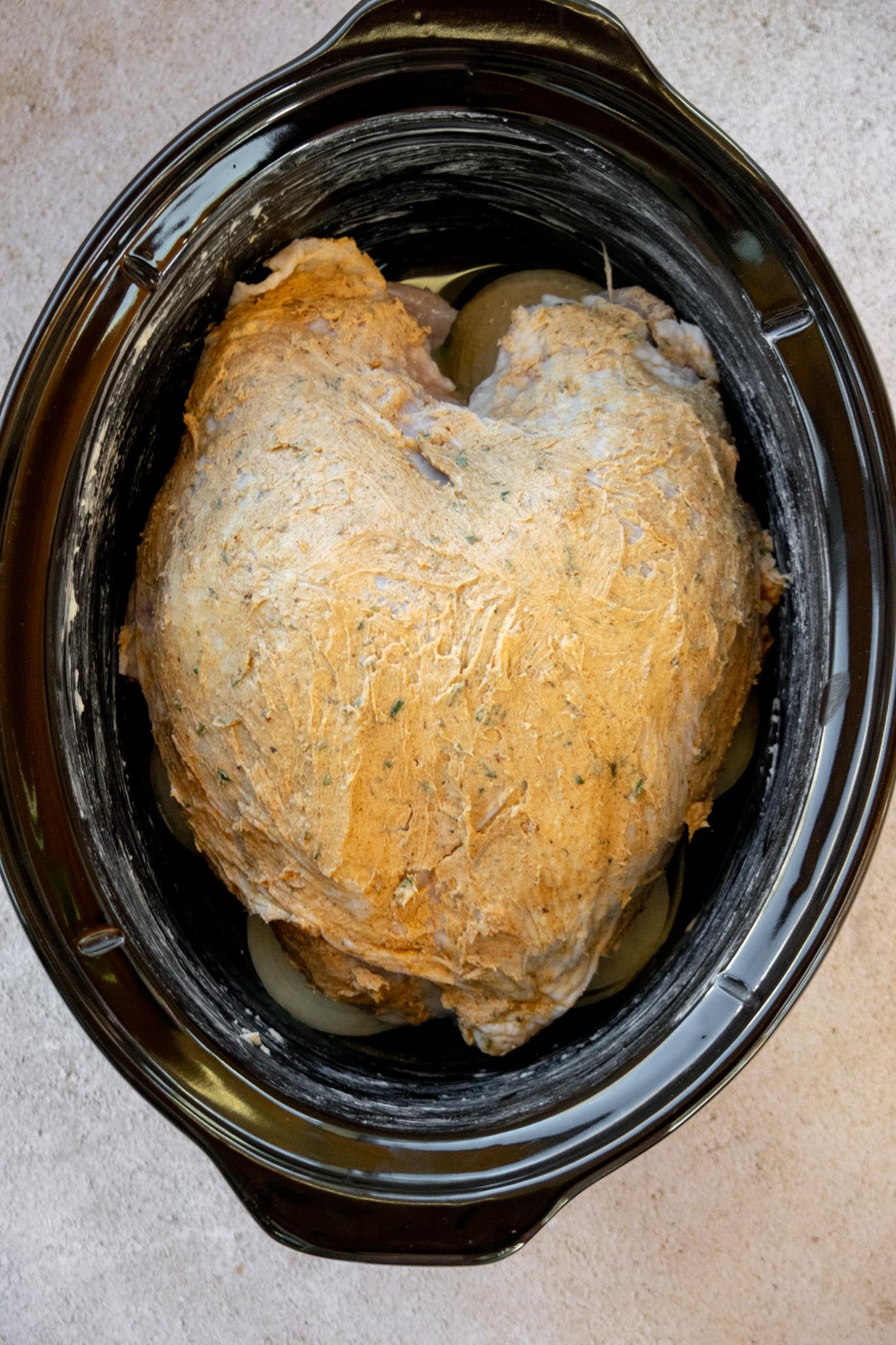 Prepare the slow cooker. Grease the slow cooker, then add the sliced onions, crushed garlic, and chicken stock. Place the turkey breast on top, skin-side up.