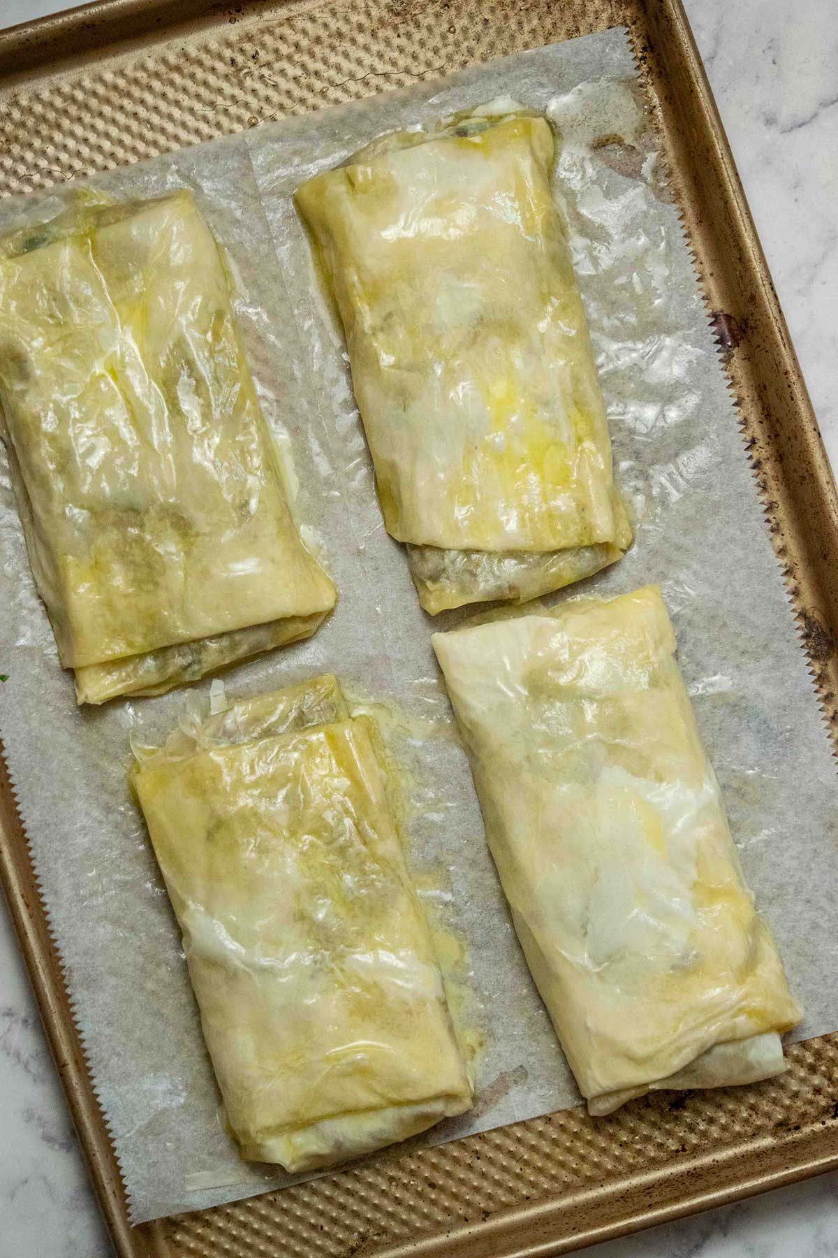 Roll and seal. Use the parchment paper to help roll the pastry over the filling into a sealed strudel, tucking in the sides as you go. Repeat with the remaining phyllo and filling, then place the strudels seam-side down on the baking sheet.