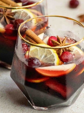 Close-up of fall sangria in a glass garnished with fresh cranberries, lemon slices, cinnamon sticks, and star anise, with a second glass in the background.