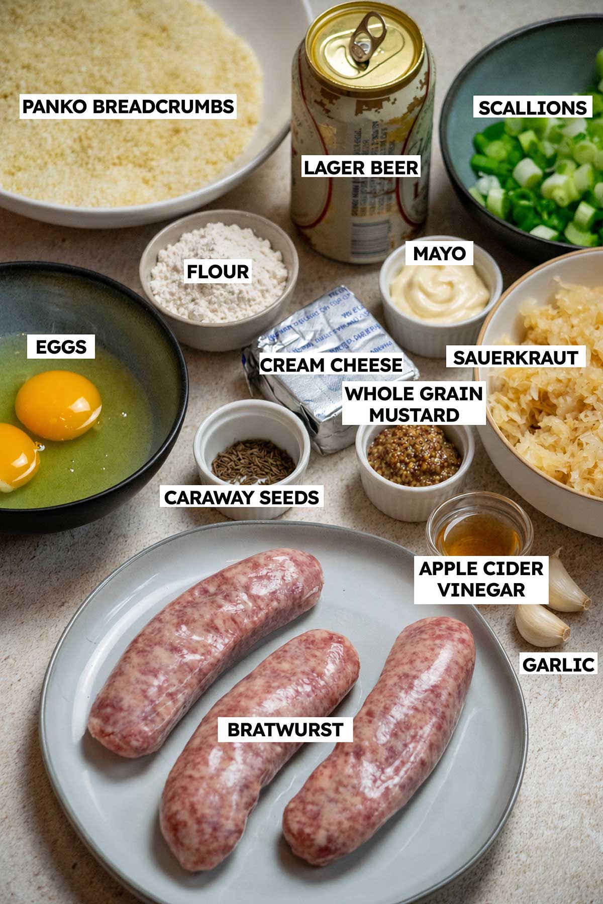 Ingredients for crispy sauerkraut balls, including bratwurst, sauerkraut, panko breadcrumbs, eggs, cream cheese, beer, scallions, caraway seeds, flour, mayonnaise, whole grain mustard, apple cider vinegar, and garlic.