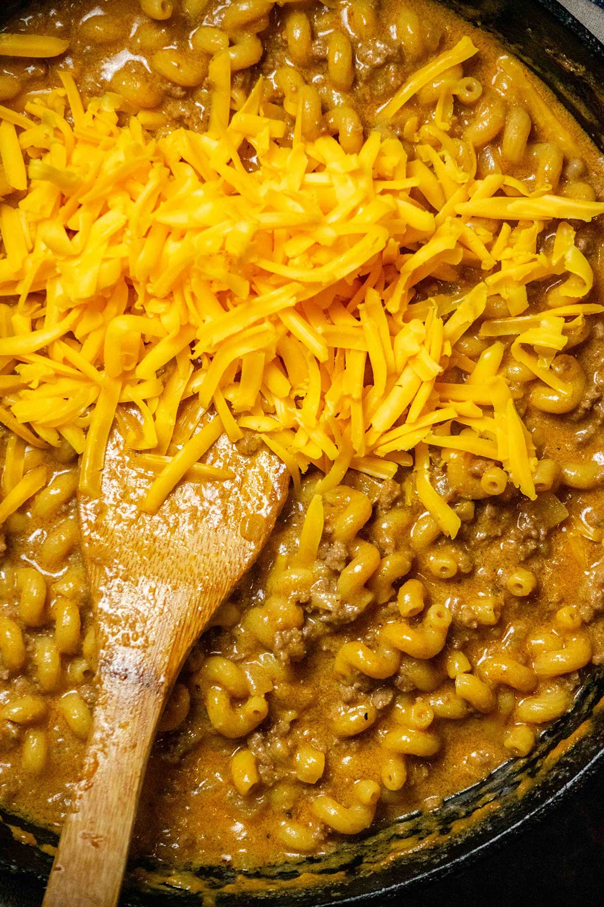 Add the cheese off heat. Remove the pan from the heat, then stir in the freshly grated cheddar until smooth and creamy. Let the Cheeseburger Helper rest for 3–5 minutes before serving.