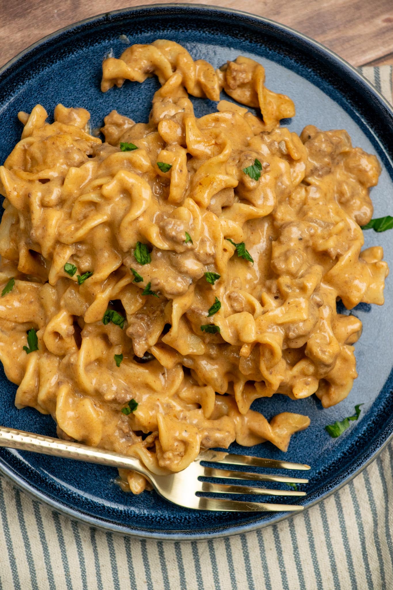 Overhead view of Homemade Hamburger Helper Beef Stroganoff with ground beef, egg noodles, creamy sauce, and chopped parsley on a blue plate.