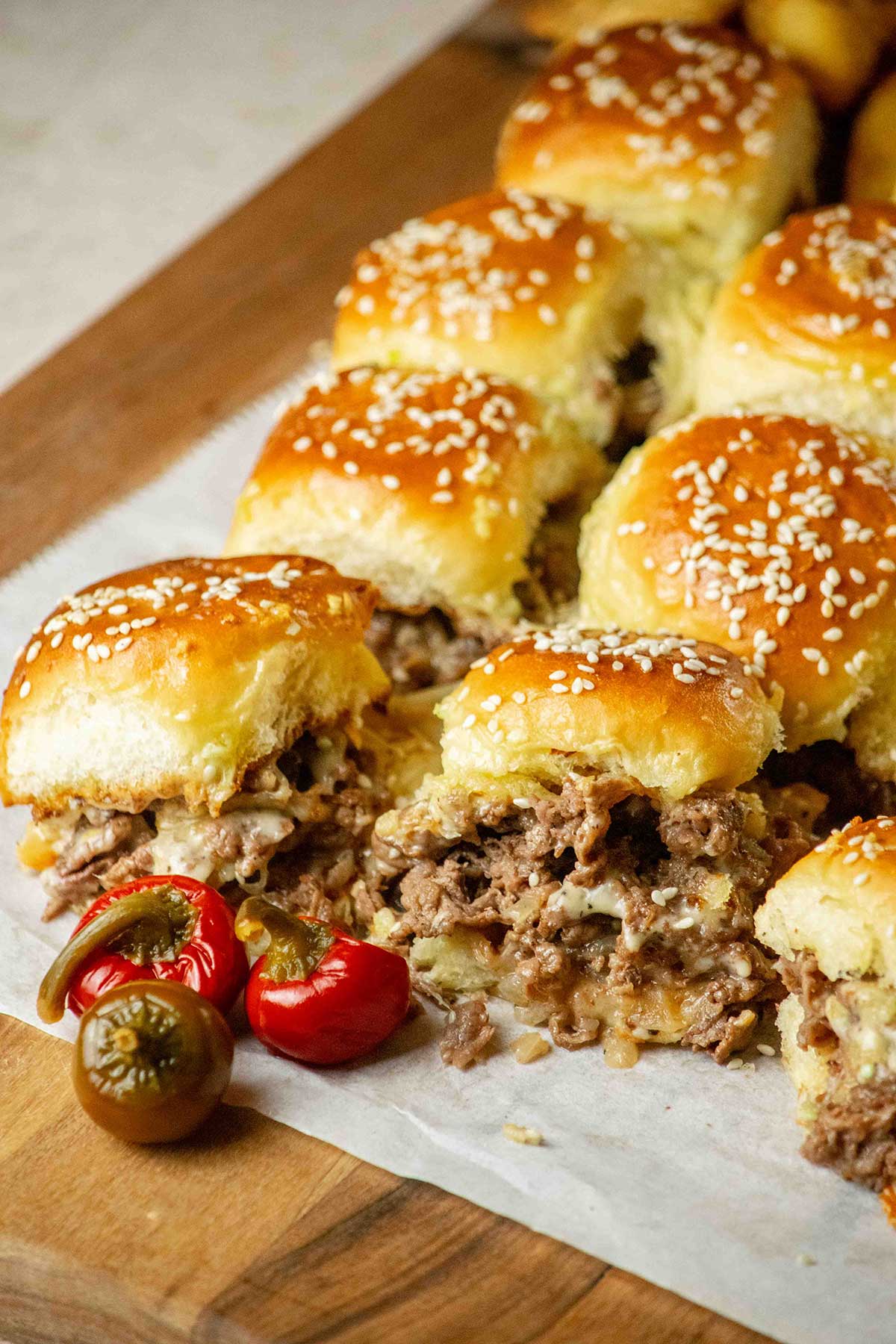 Tray of baked Philly cheesesteak sliders with golden sesame-topped rolls, melted cheese and shaved steak filling.