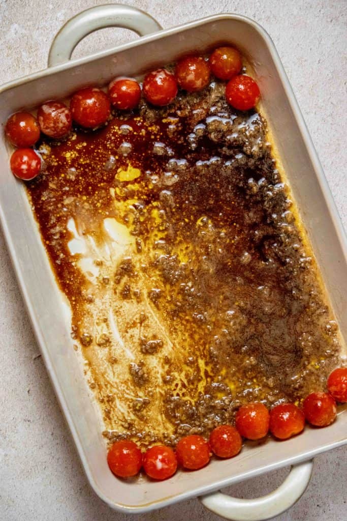 grease a large baking dish, then add the tomatoes, balsamic, olive oil and garlic, toss well, and push to ends of dish 