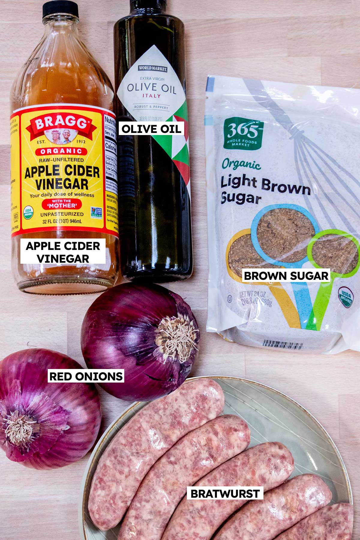Oven baked brats ingredients- bratwurst, red onions, brown sugar, salt, pepper, and olive oil in a bowl.