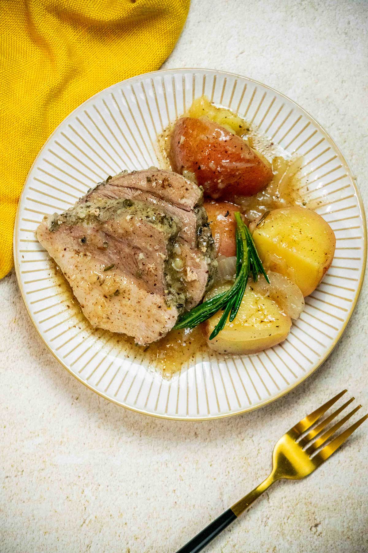 Plated slow cooker pork sirloin roast with red potatoes, onions, gravy, and fresh rosemary.