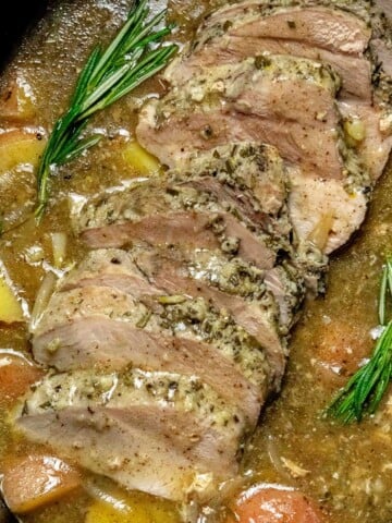 Slow cooker pork sirloin roast sliced in gravy with red potatoes, onions, and fresh rosemary.