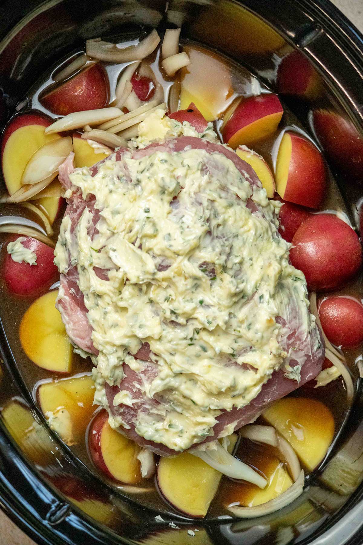 Assemble the slow cooker. Add the red potatoes, sliced onion, chicken stock, and balsamic vinegar to the crockpot. Place the seasoned pork roast on top.