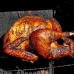Whole smoked turkey with crispy, deeply browned skin cooking on a rack in an electric smoker.