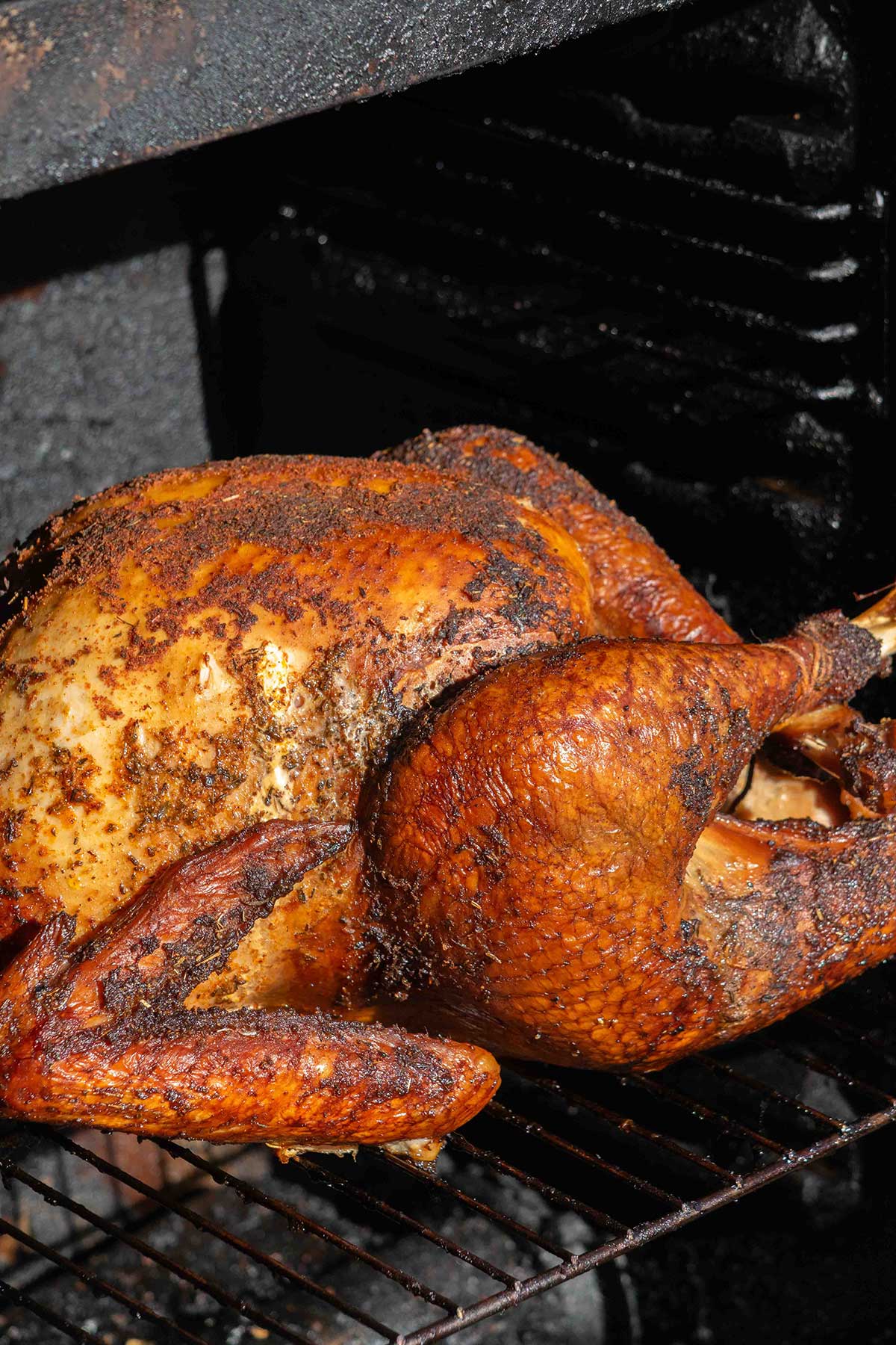 Close-up of whole smoked turkey with smoky, golden brown skin and seasoned breast and legs.